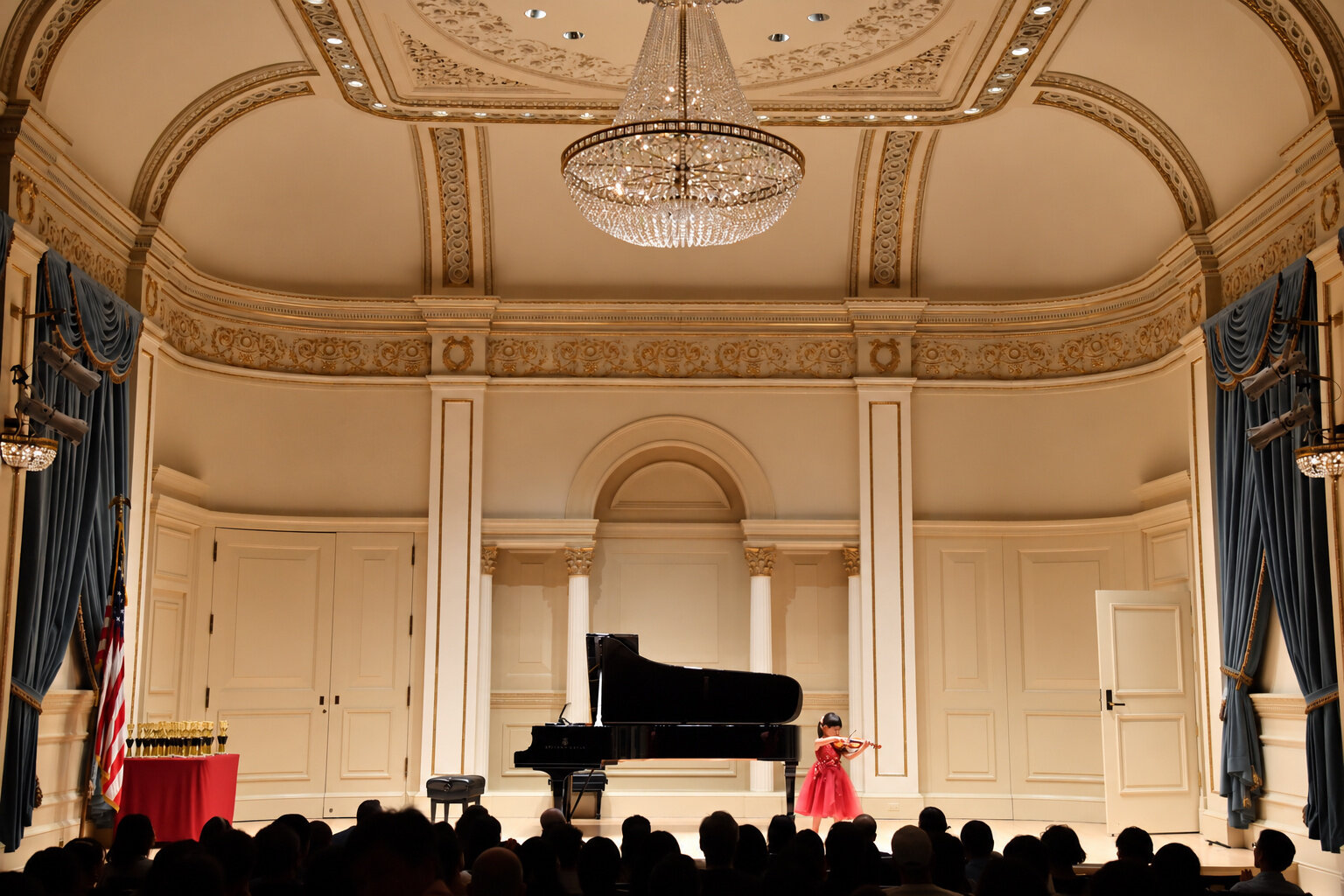 Hailey Murata performing solo in a formal recital hall with trophies displayed